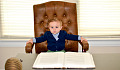 young boy sitting in a big leather chair in front of a business desk